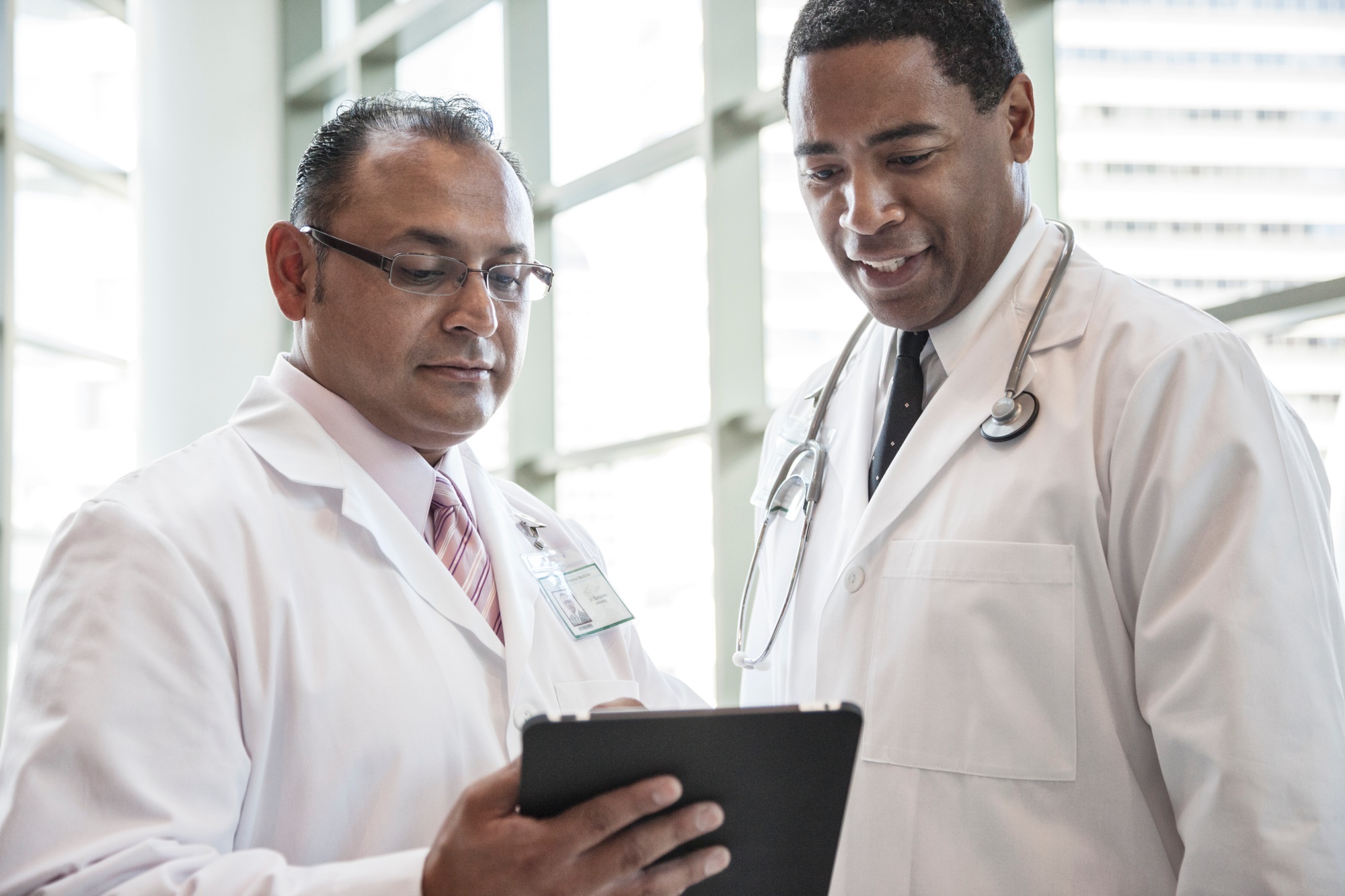 Black and Hispanic male doctors discussing a case in a hospital hallway.