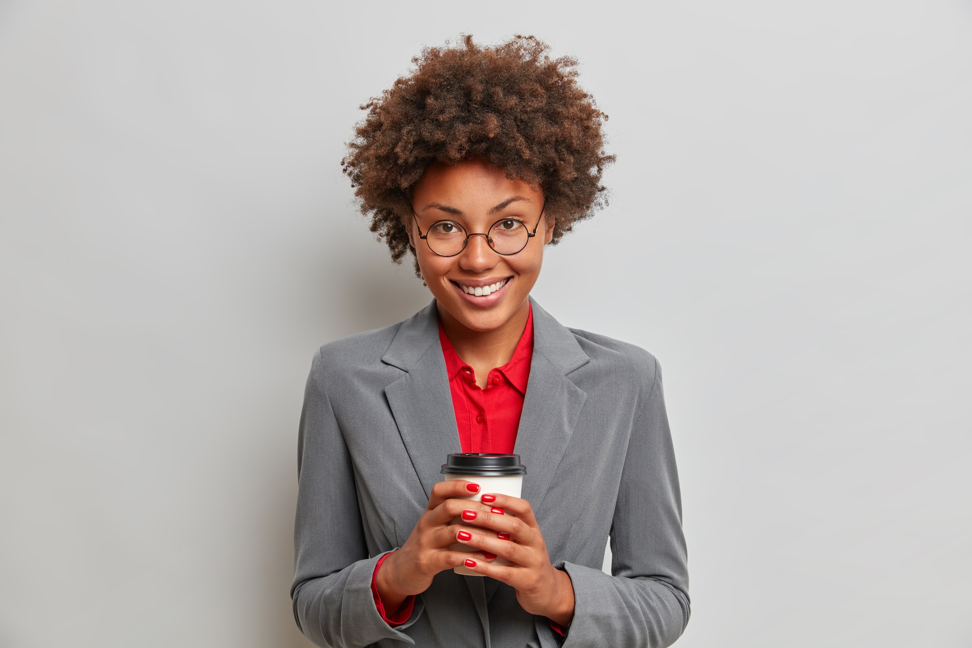 Positive female administrative assistant in formal outfit, has cheerful expression, enjoys coffee br